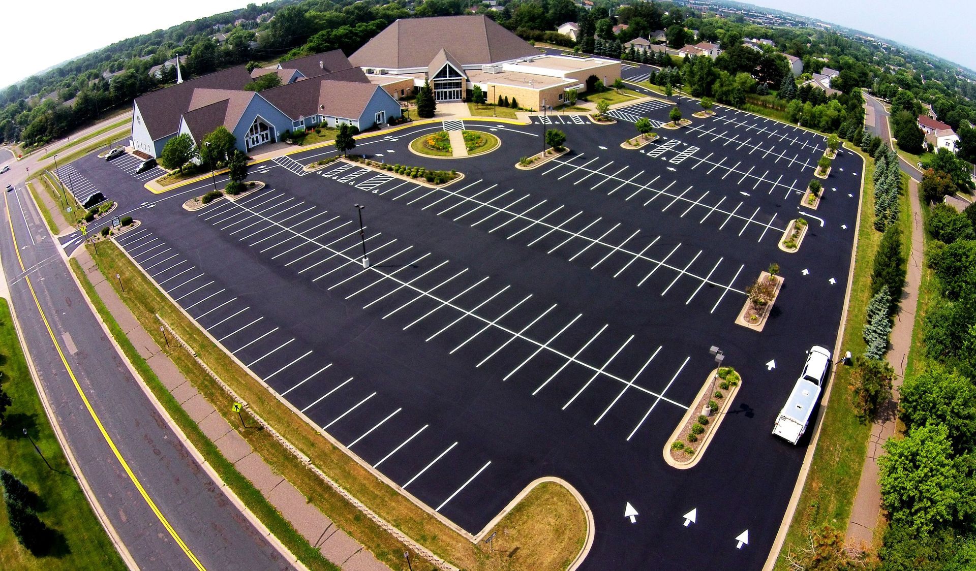 Aerial view of a nearly empty parking lot beside a large building complex on a sunny day