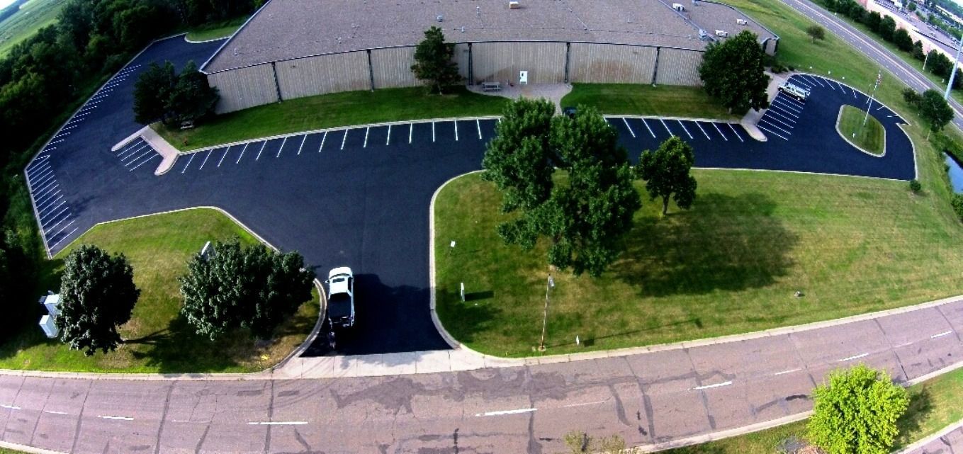 Aerial view of a parking lot with a few cars, trees, and surrounding roads