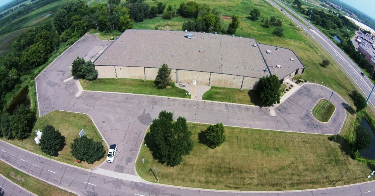 Aerial view of a large beige building with parking lot, trees, and grassy grounds.