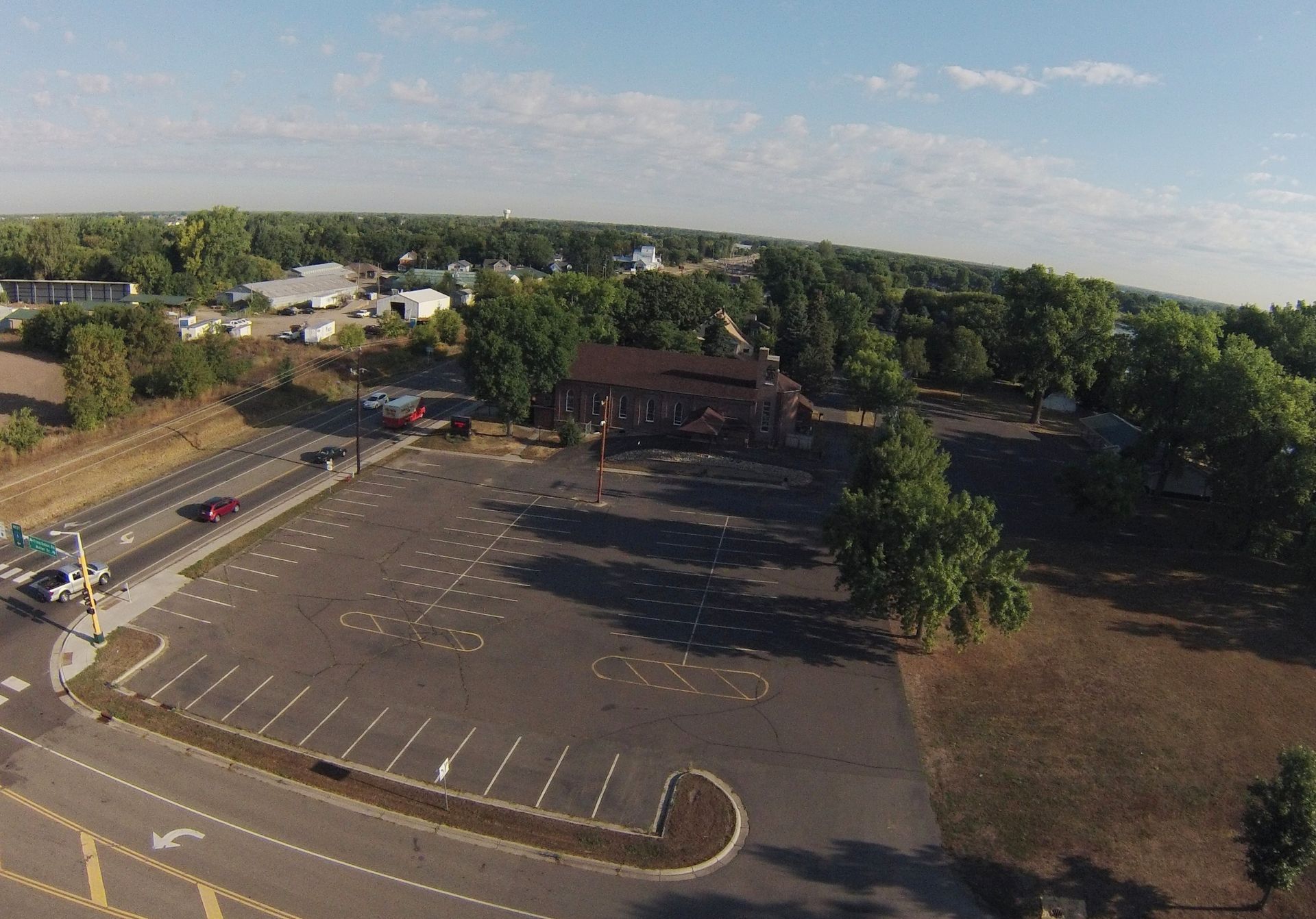 Aerial view of mostly empty parking lot beside a brick building and trees on a sunny day