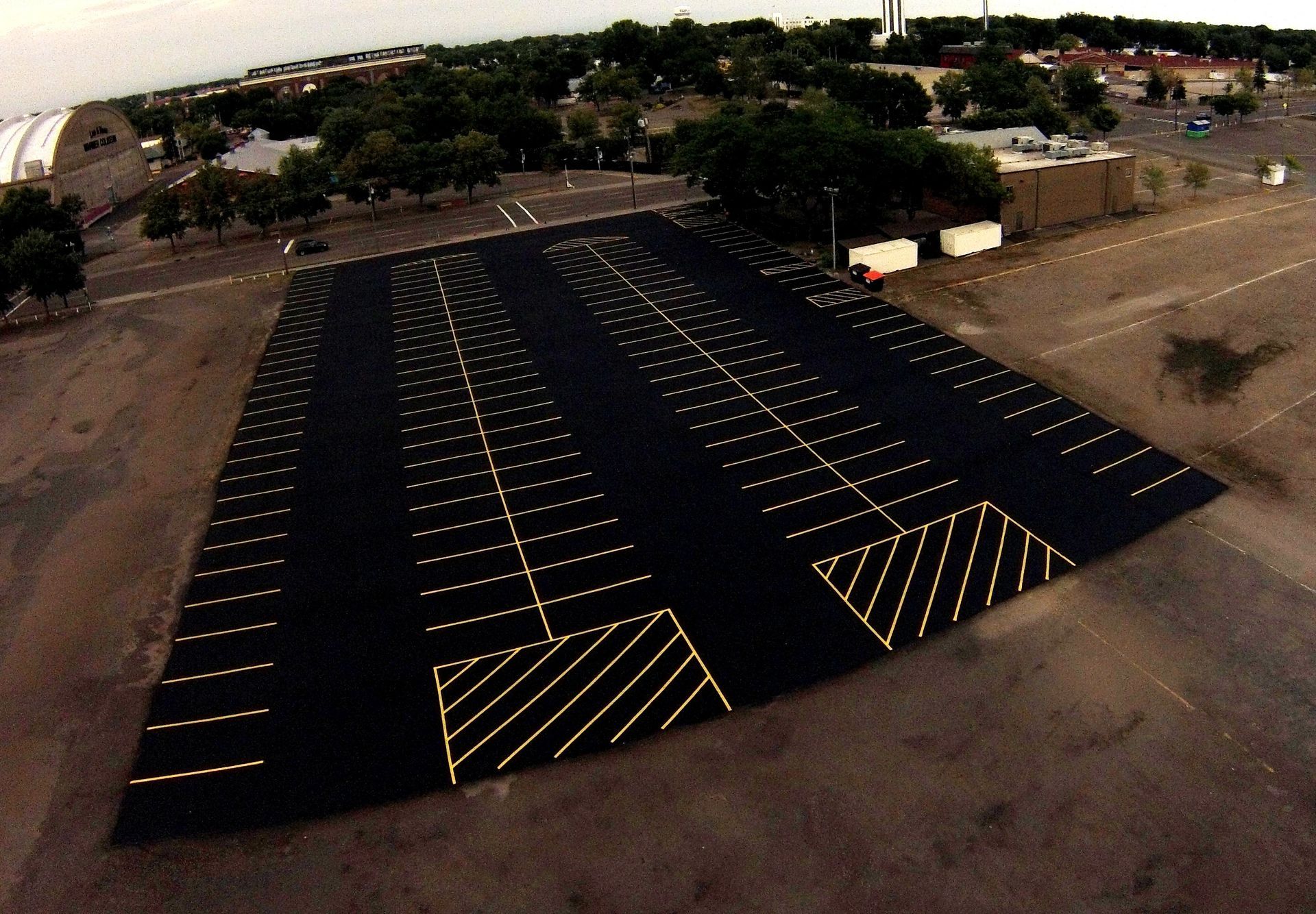 Large black solar panel array in a dirt lot with striped yellow markings, viewed from above.