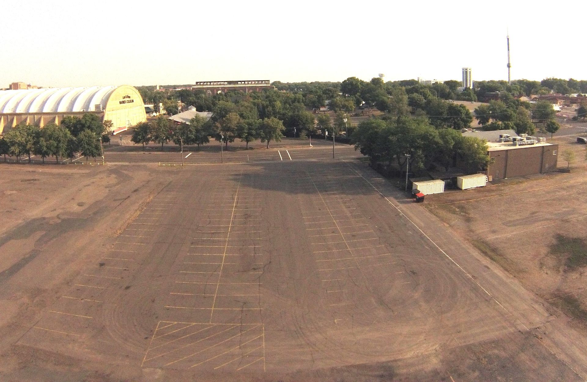 Empty dirt lot beside buildings and trees under a clear sky