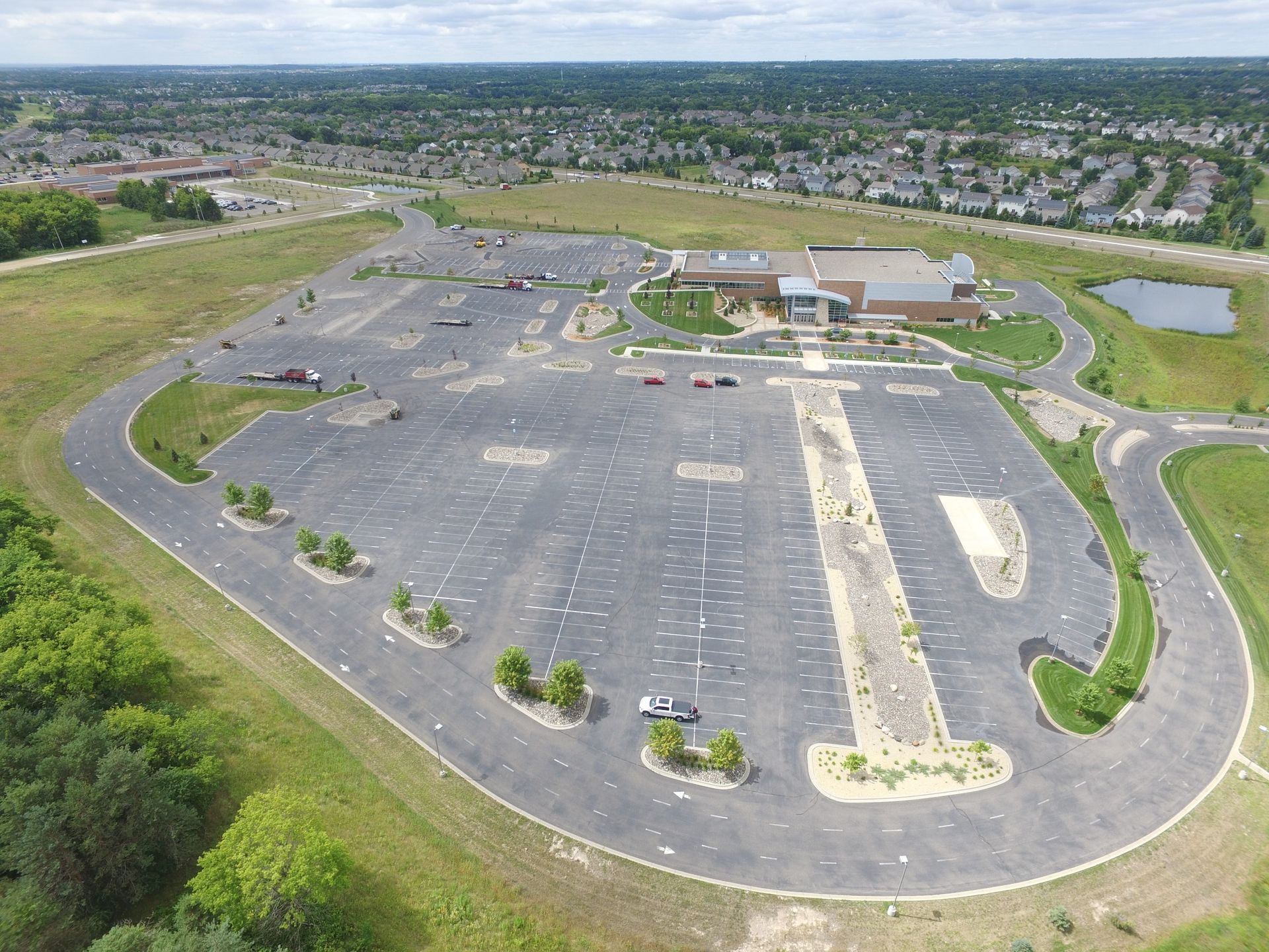 Aerial view of a large empty parking lot beside grassy fields and suburban homes.