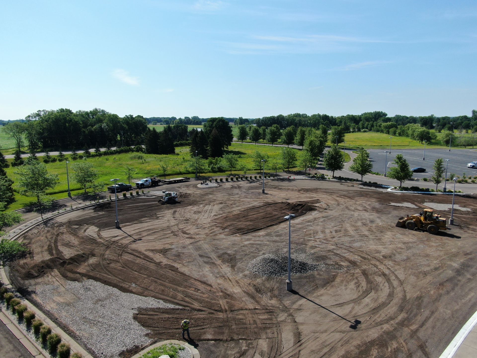 Aerial view of a large dirt construction site with machinery, surrounded by trees and open fields.