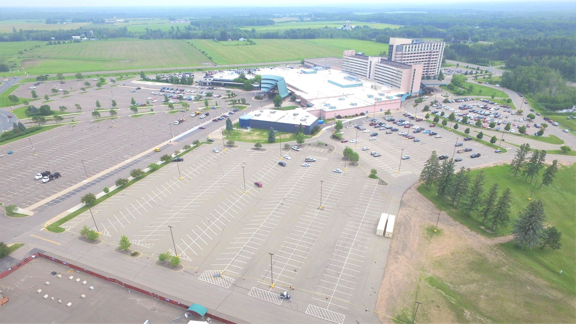 Aerial view of a large parking lot beside a stadium or arena, with many empty spaces and surrounding greenery