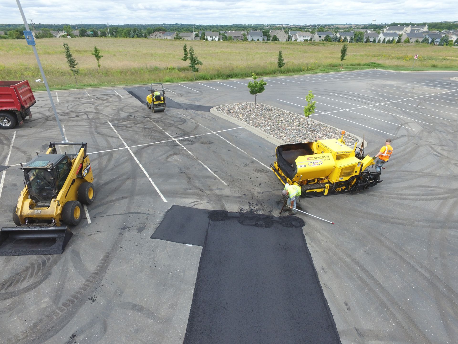 Parking lot with yellow construction equipment and a dark pavement patch under repair