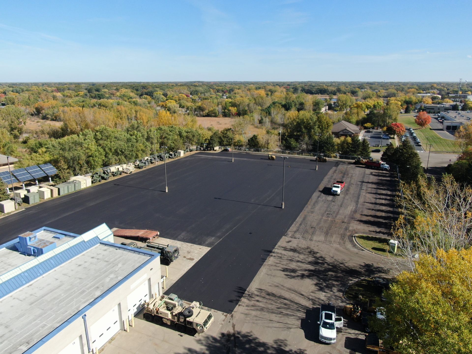 Aerial view of a large empty black parking lot beside buildings and trees in autumn.