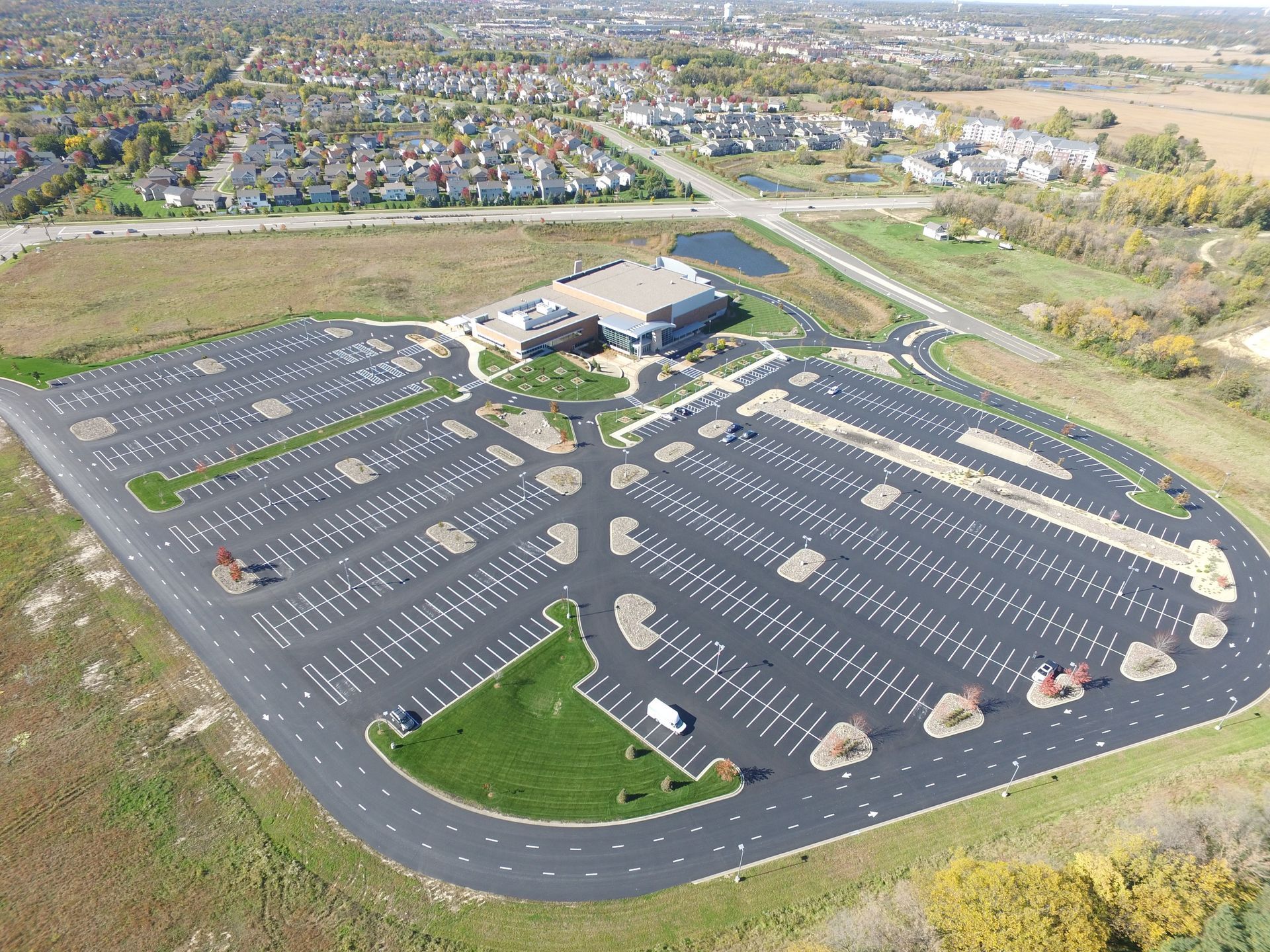 Aerial view of a mostly empty parking lot beside a building, with a suburban neighborhood in the background