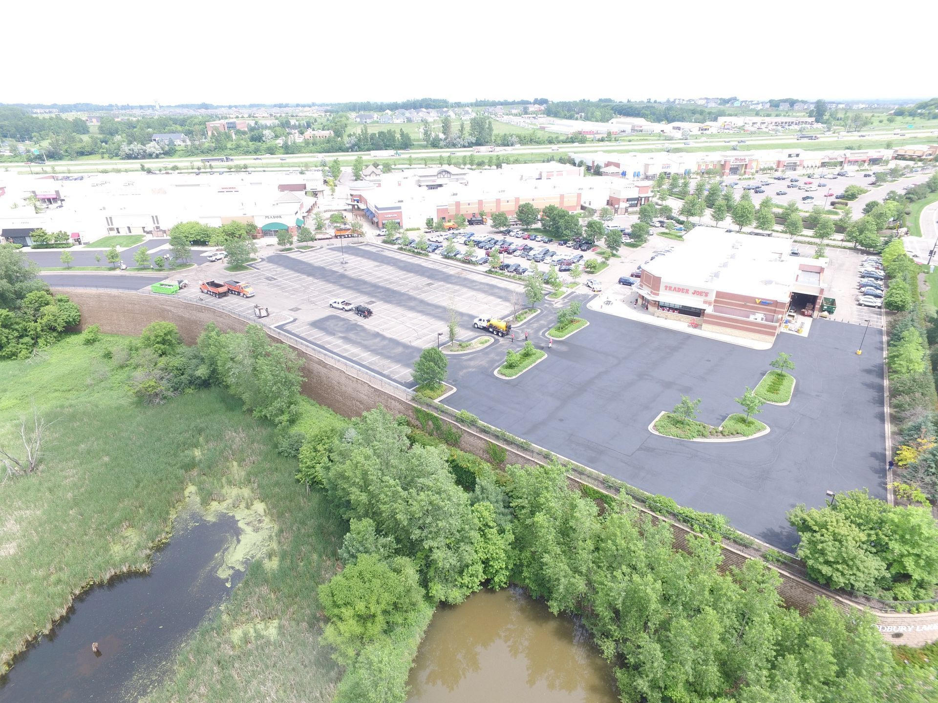 Aerial view of a parking lot beside a building, trees, and a small pond.