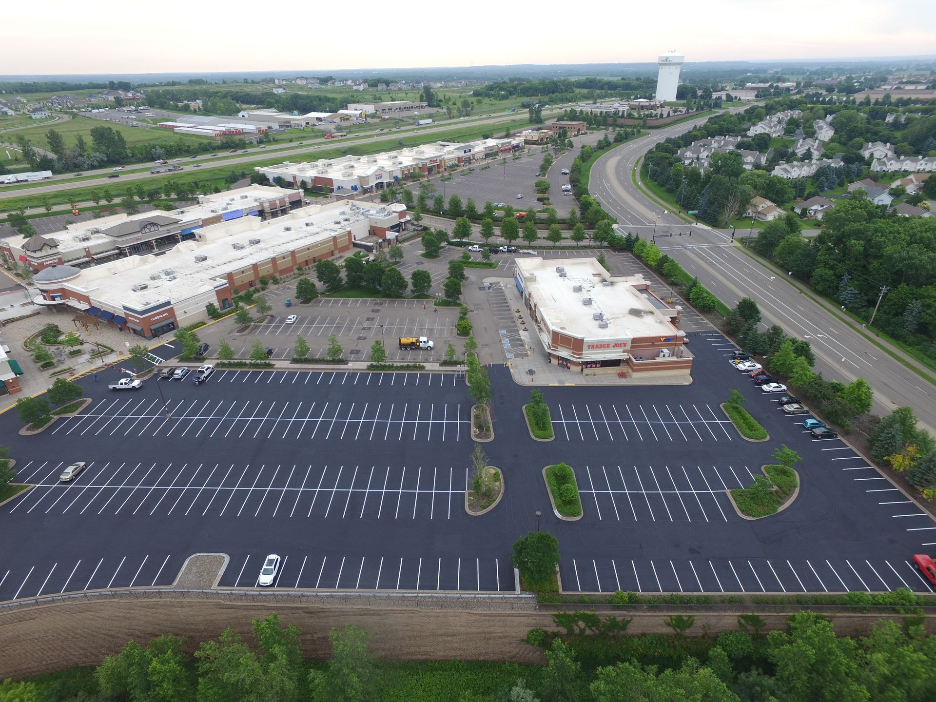 Aerial view of a large empty parking lot beside a shopping center and curving road.