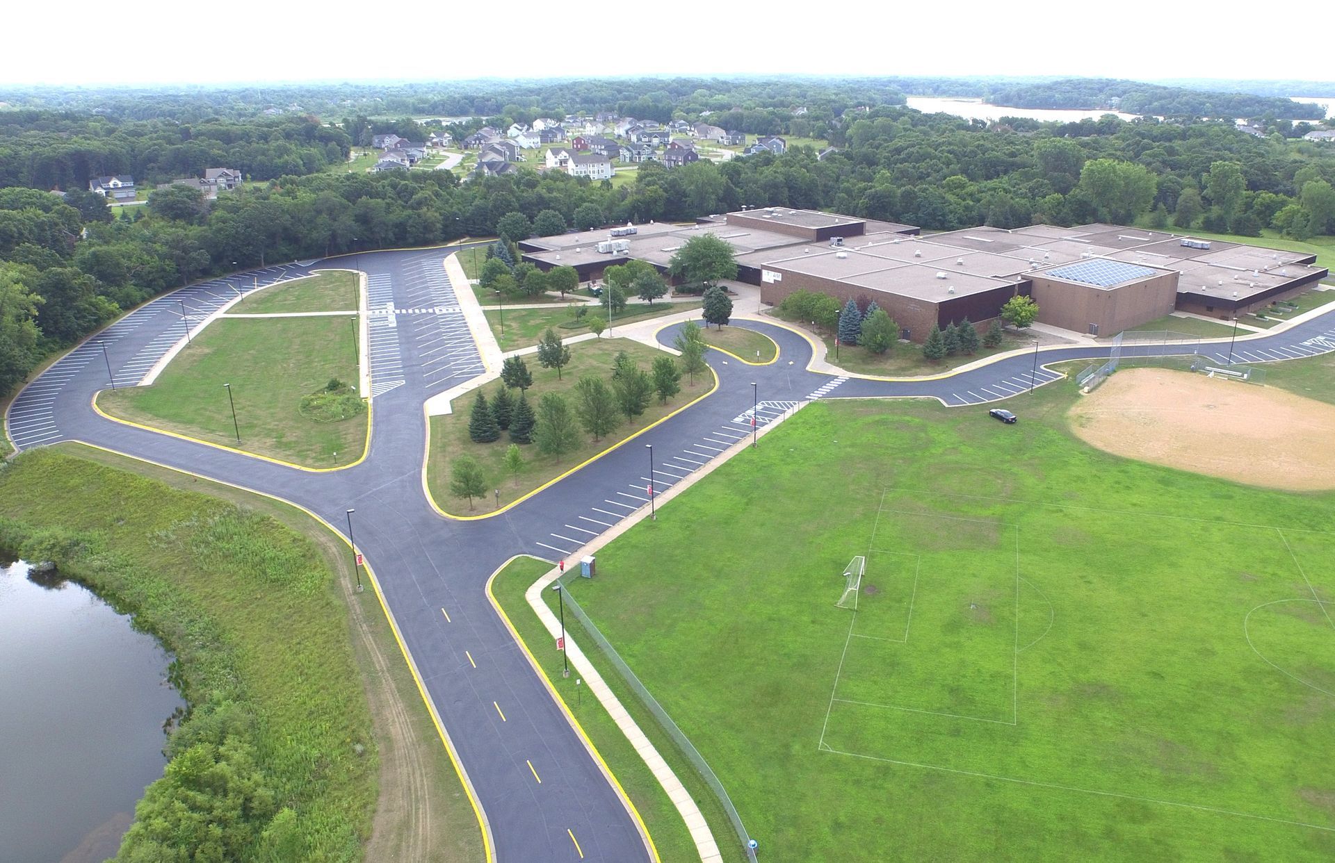 Aerial view of a school campus with parking lots, green fields, and a baseball diamond.