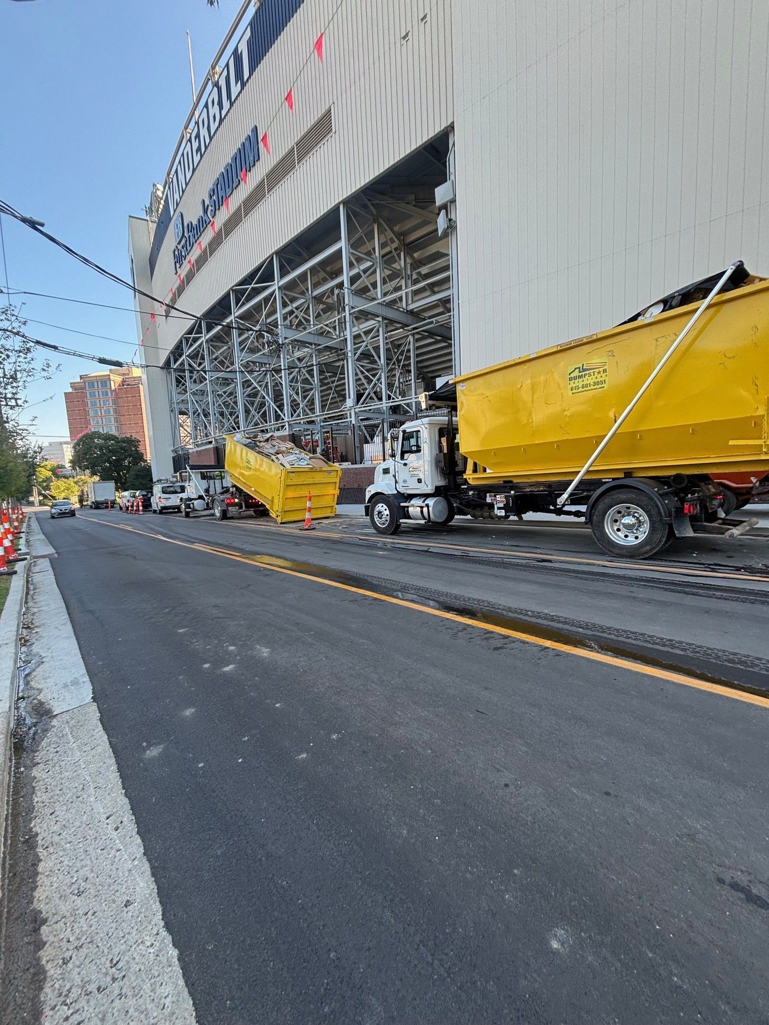 Yellow dump trucks unloading debris near a large building with metal scaffolding. Asphalt road.