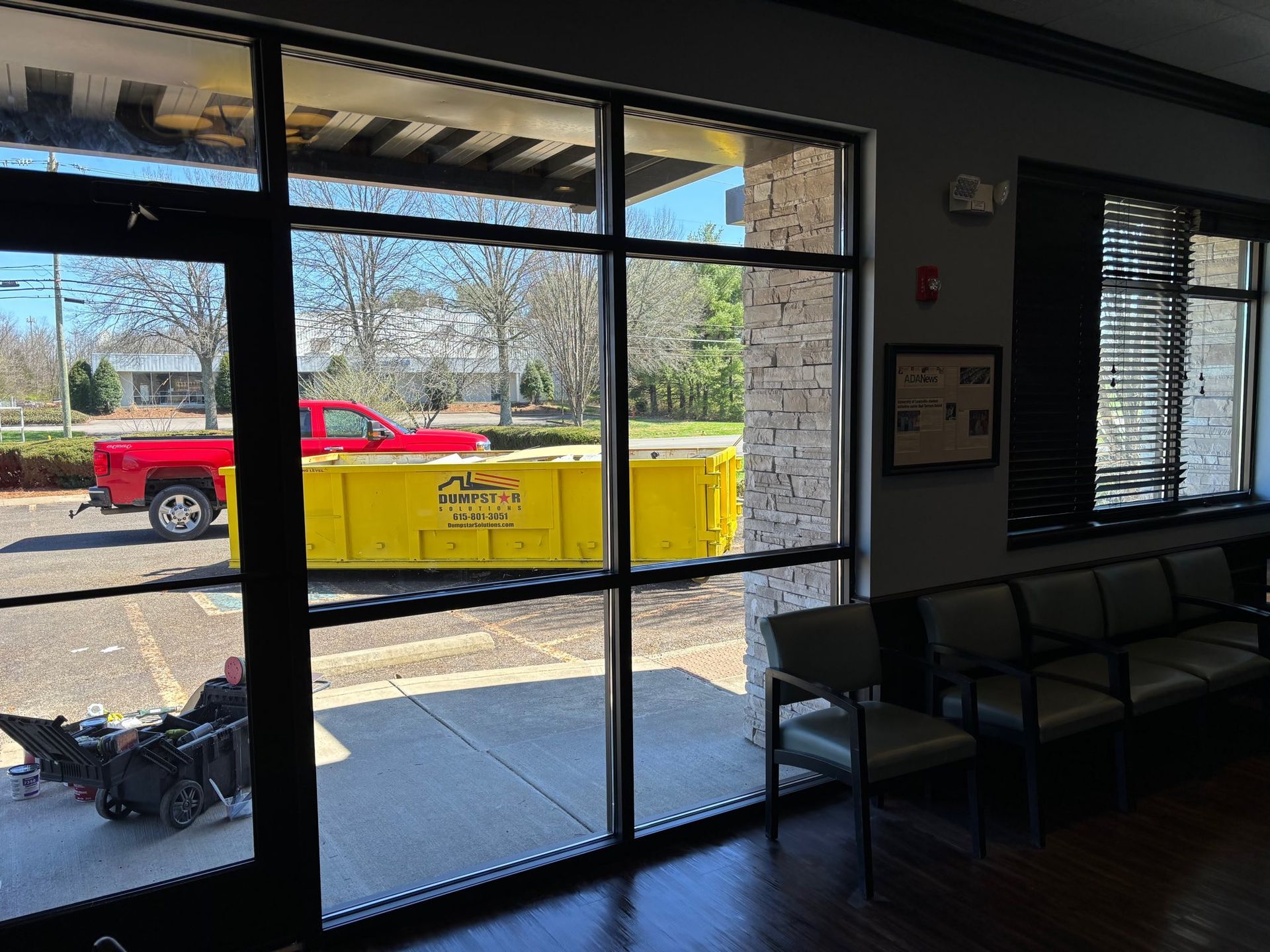 Interior view of a waiting room with large windows overlooking a parking lot with a red truck and yellow dumpster.