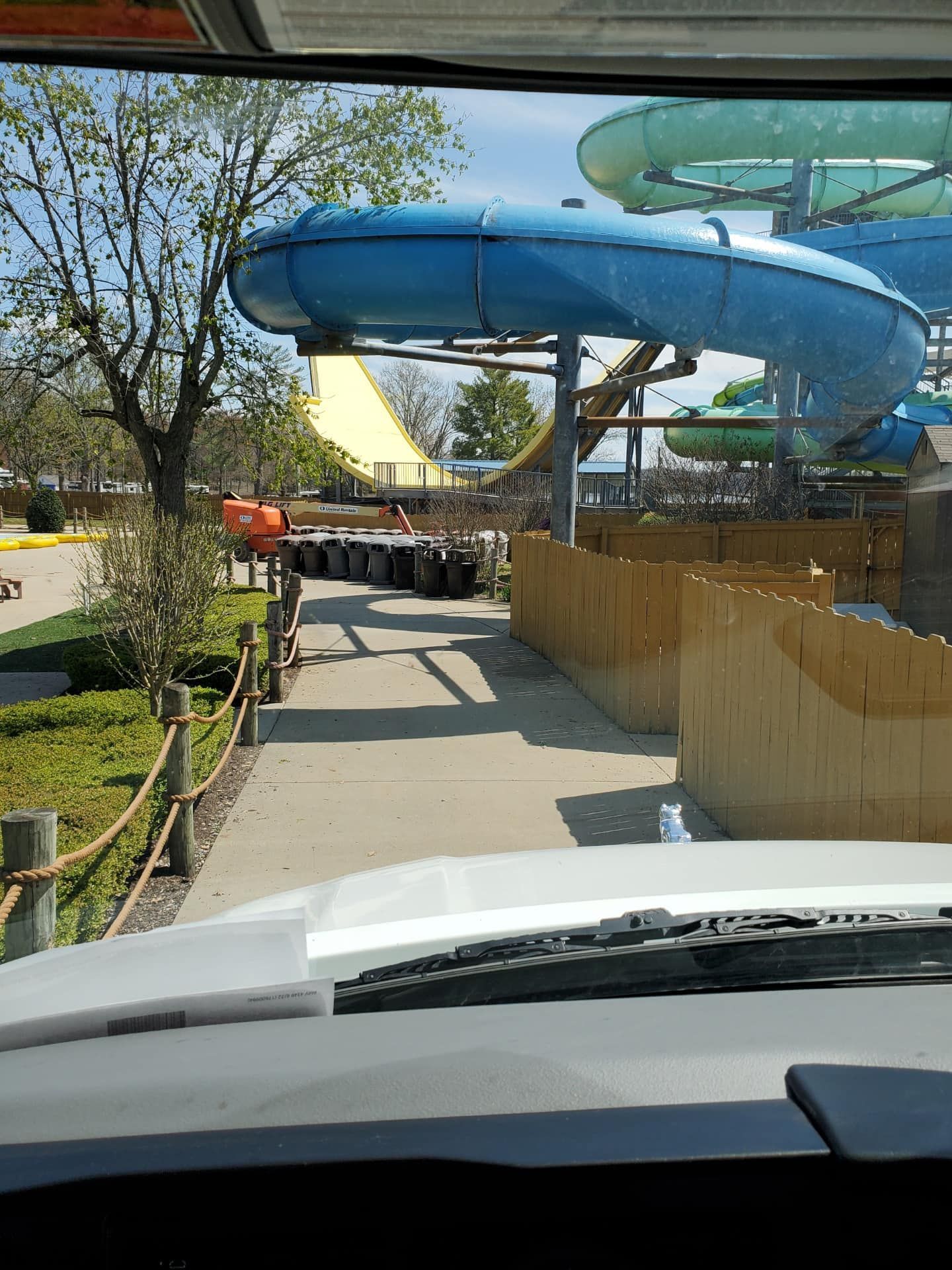 View from a vehicle of a waterpark with blue and yellow slides, a wooden fence, and a walkway.