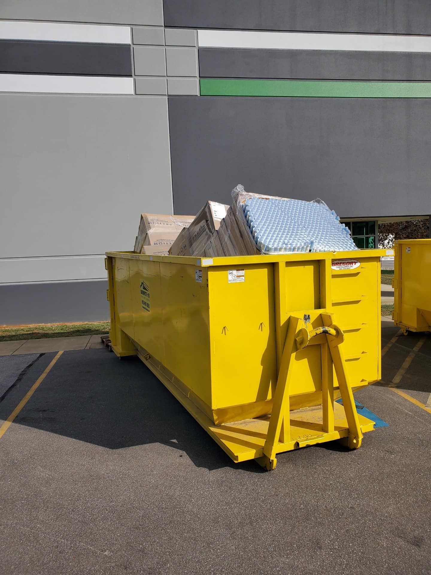 Yellow dumpster overflowing with mattresses outside a building.