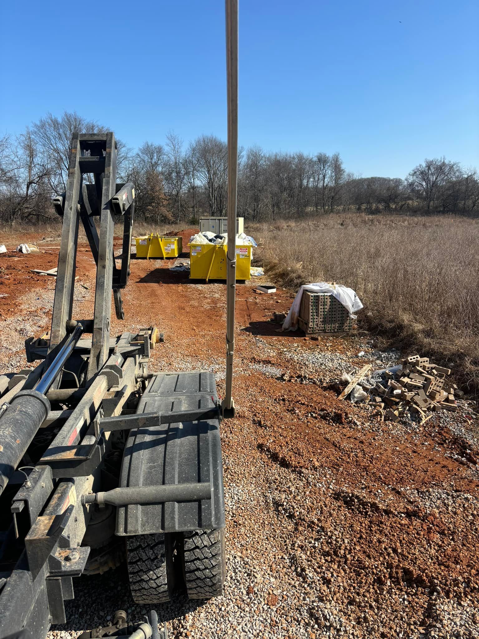 A drilling rig with a vertical pipe on a construction site, near a pile of rocks and containers.