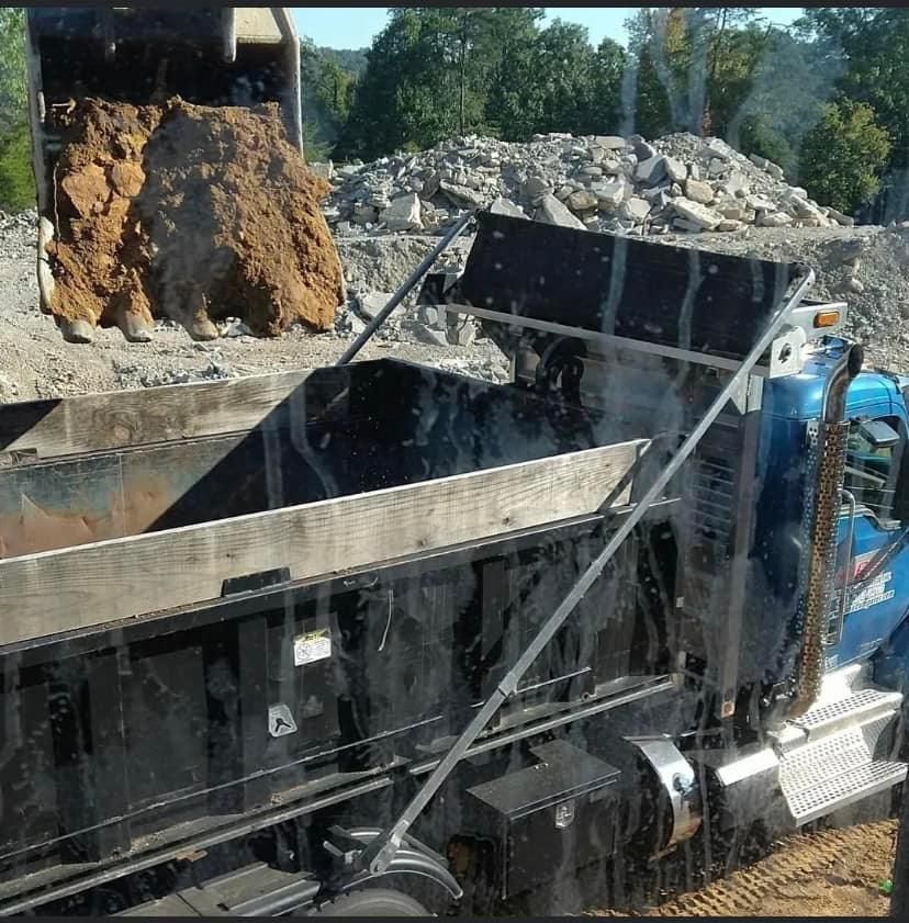 A dump truck being loaded with dirt by a backhoe at a construction site.