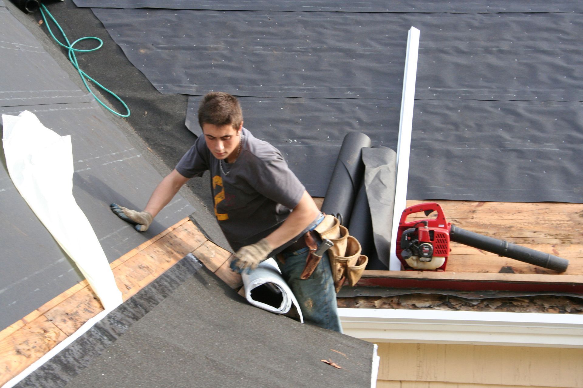 Roofer installing roofing material on a house, using a blower.