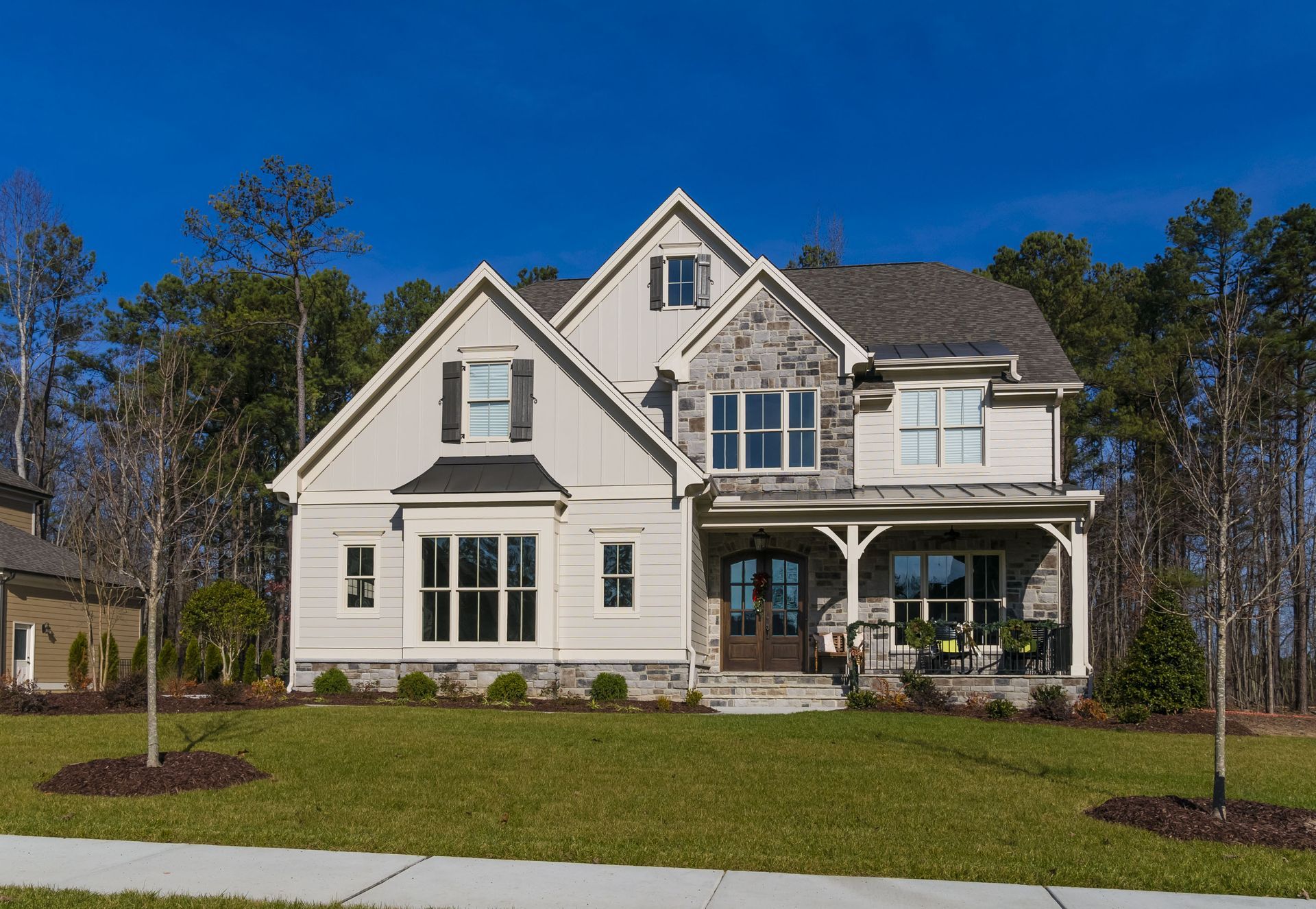 Two-story beige house with stone accents, porch, and a well-manicured lawn on a sunny day.