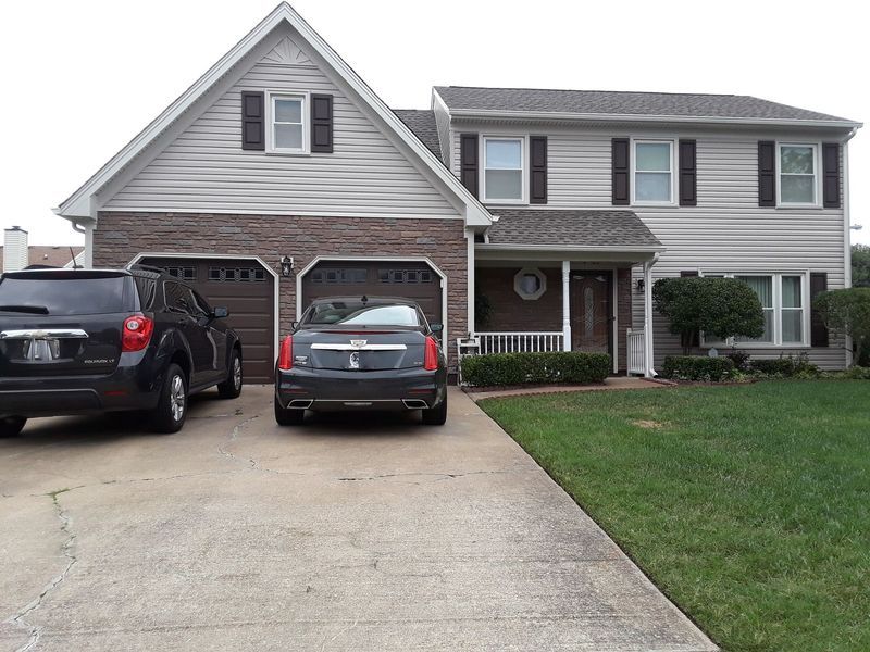 Two-story house with a brick facade and attached garage, two cars parked in the driveway, and green lawn.