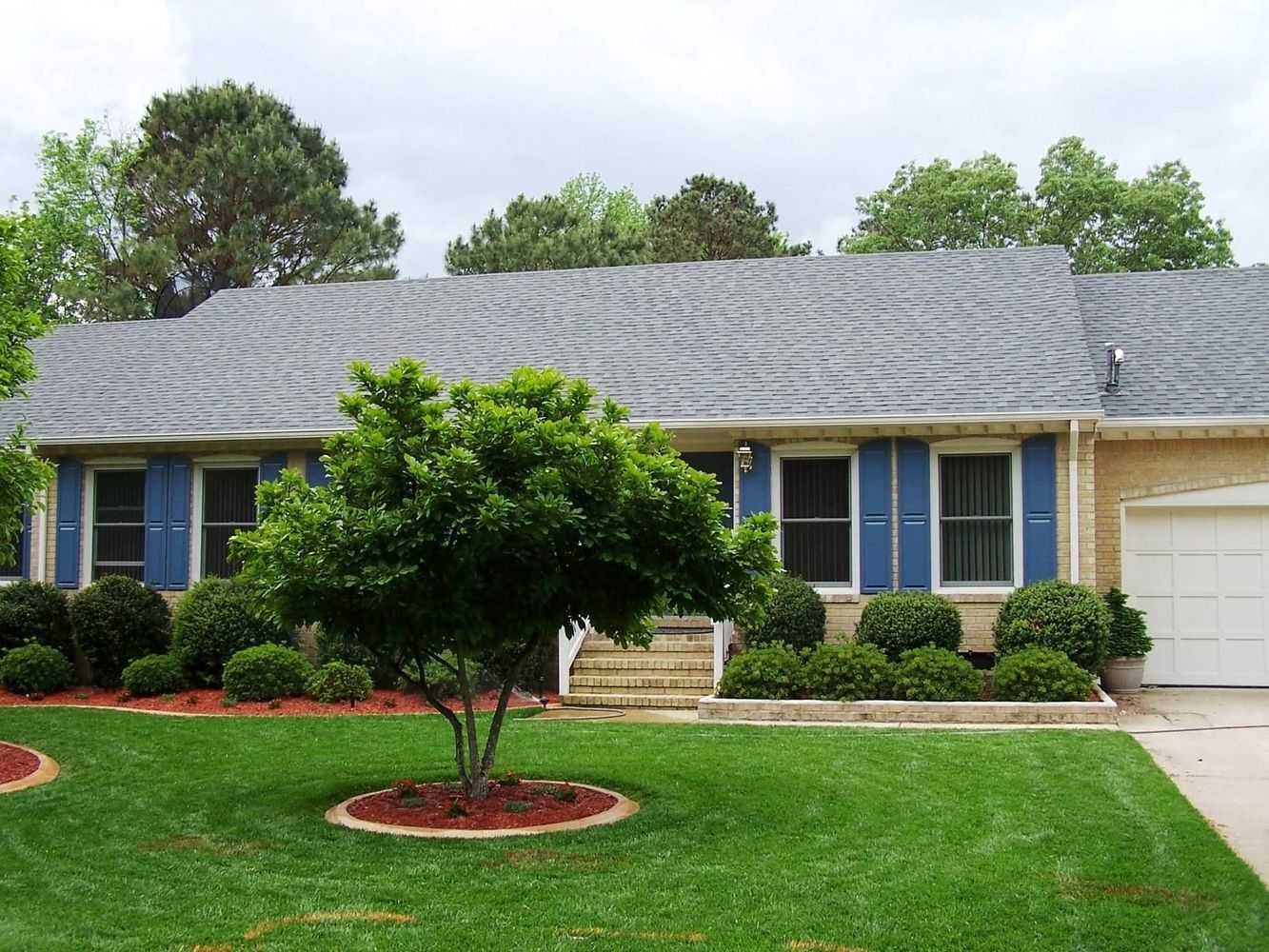 House with blue shutters, green lawn, and a tree in the yard.