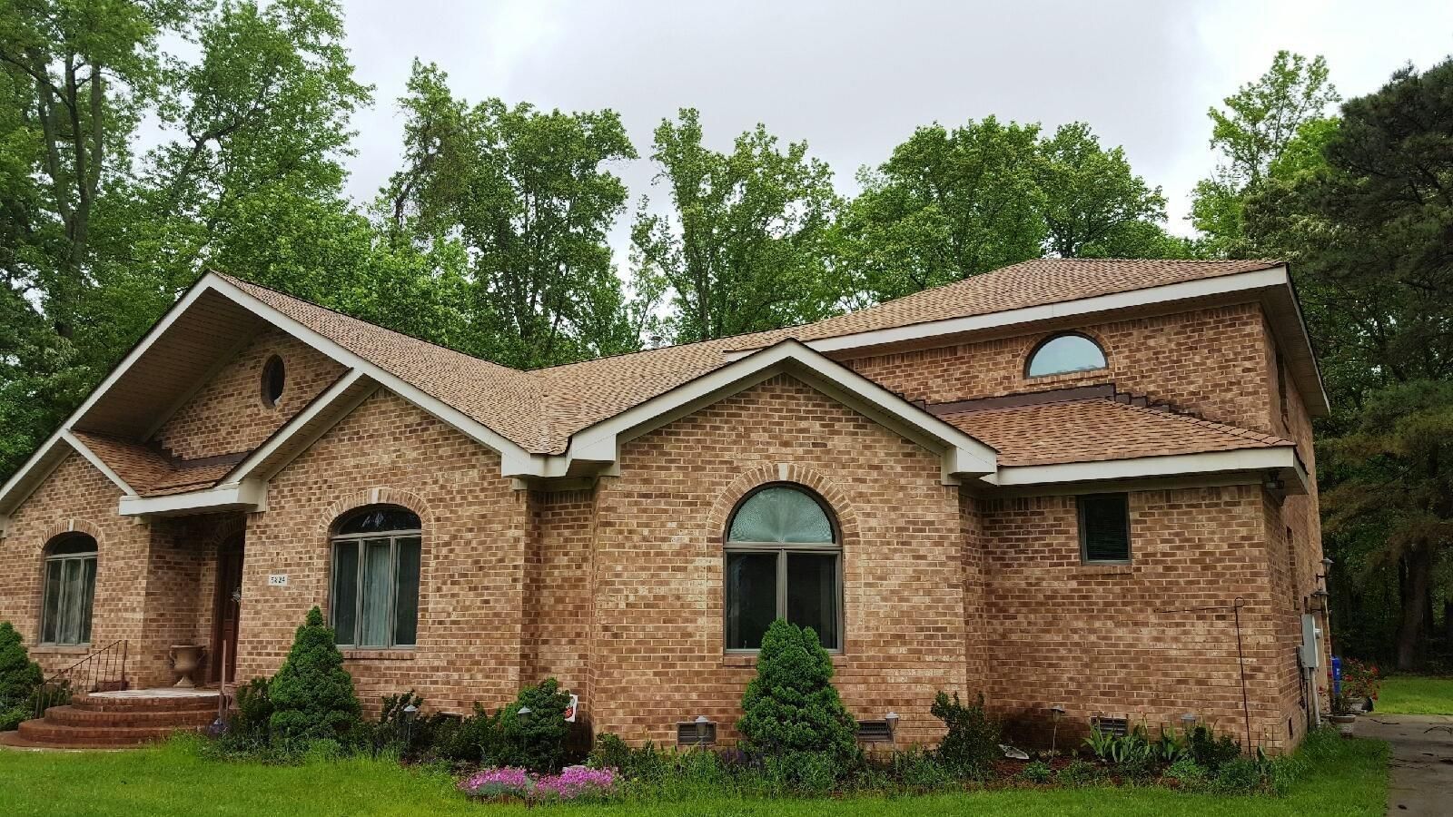 Brick house with brown roof and arched windows, surrounded by trees and green grass.