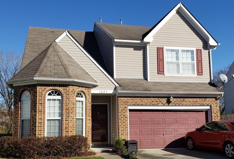 Two-story house with brick, tan siding, red garage door, and a red car parked nearby.