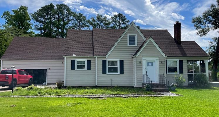 Beige house with a brown roof, black shutters, and a red truck parked in the driveway on a sunny day.