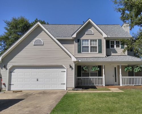 Two-story house with gray siding, white garage door, and green shutters. Front porch with hanging plants.