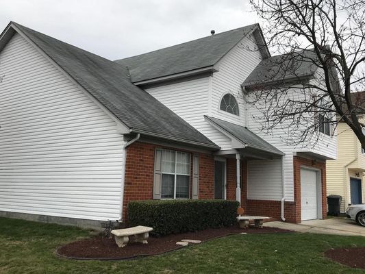 Two-story house with white siding and a dark roof. Red brick accents on the lower level. Cloudy sky.