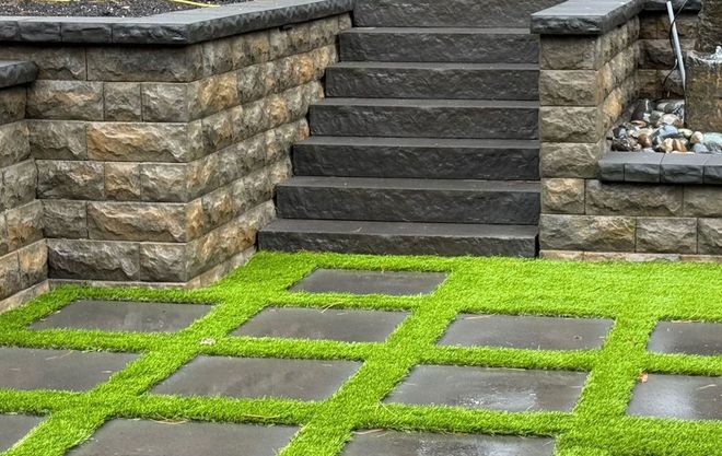 Stone steps and retaining walls next to a patio with square grass and paving stone pattern.