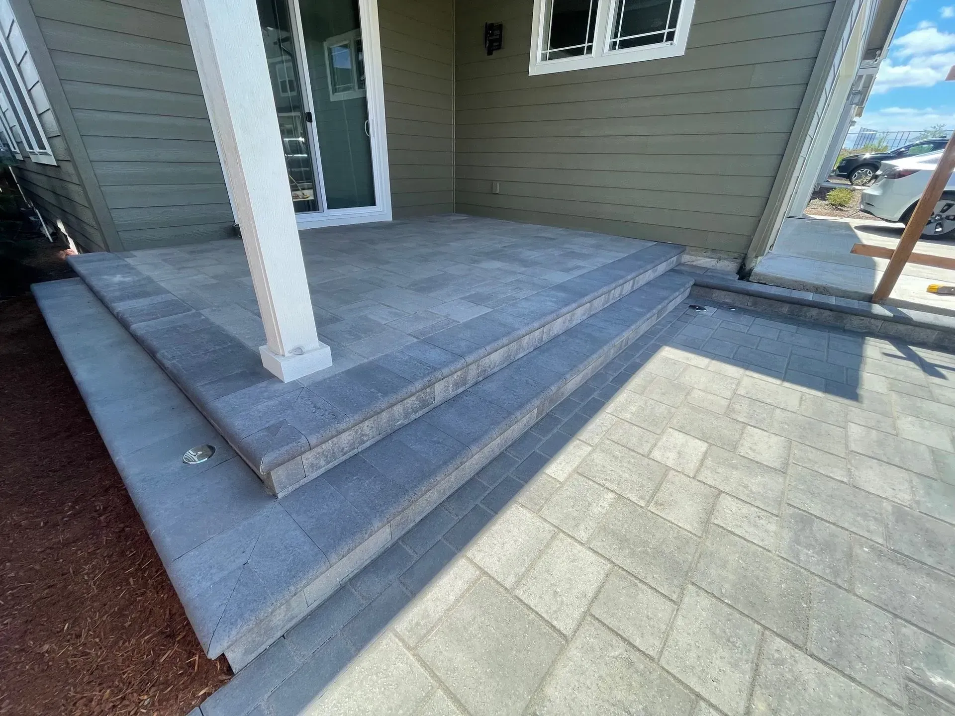 Stone steps leading to a porch with a white column, gray siding, and a glass door.