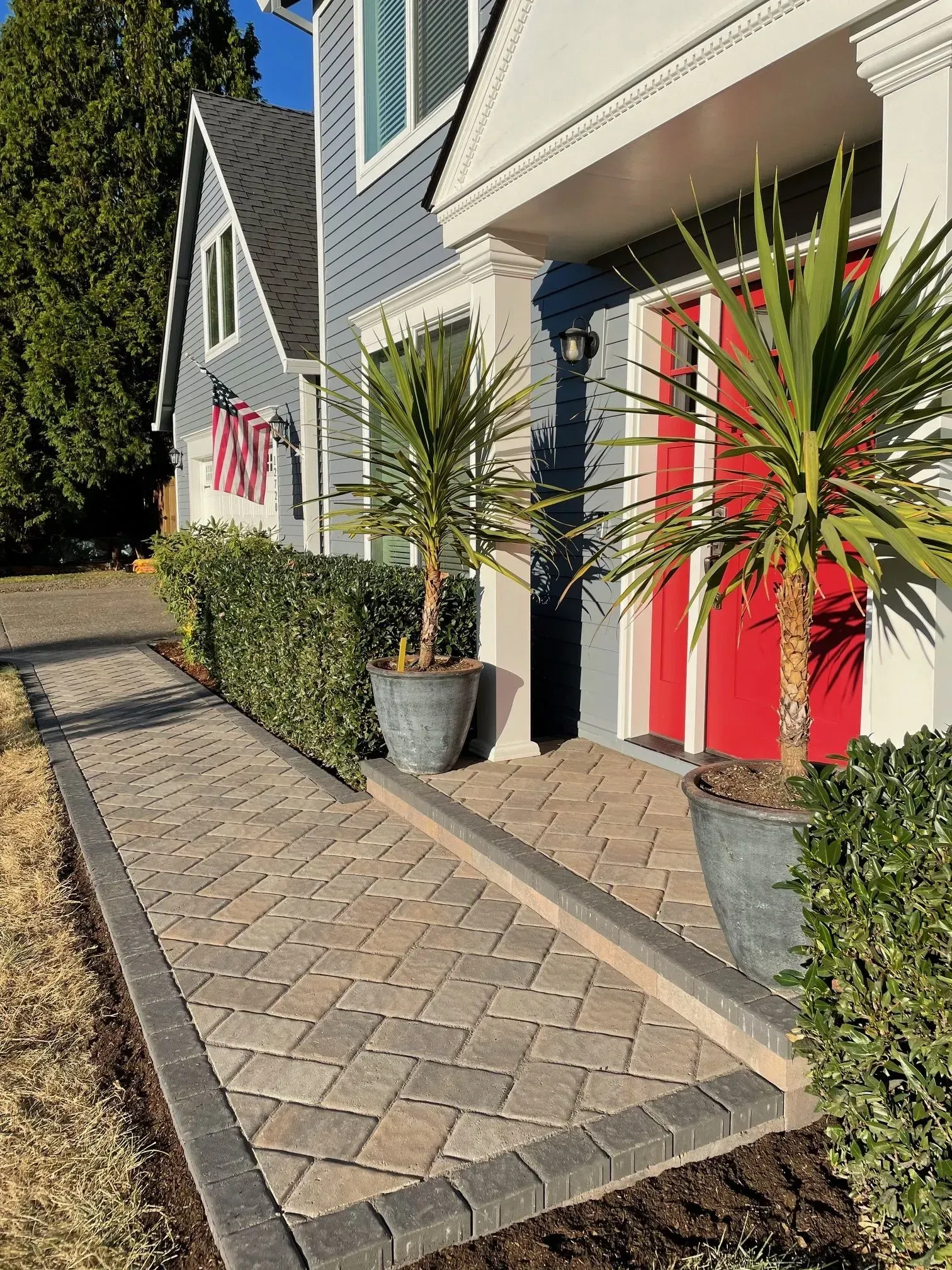Brick walkway leading to a blue house with red door. Two potted plants flank the entrance.