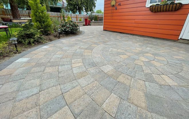 Stone patio with circular design next to orange house and garden.