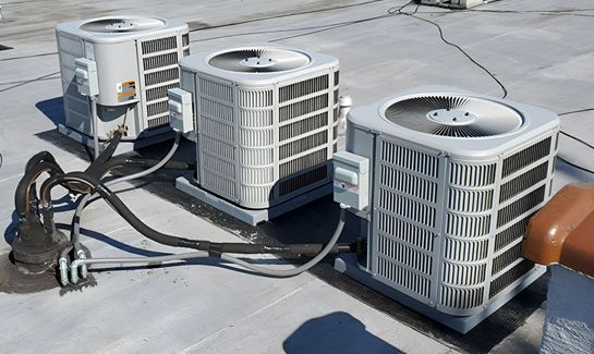 Three air conditioner heat pumps are sitting on top of a roof.