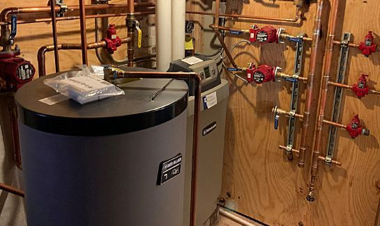 A water heater is sitting in a room with copper pipes.