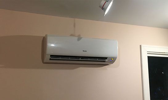 A white air conditioner is hanging on a wall next to a window.