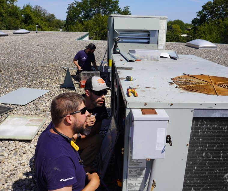 Two men are working on an air conditioner on the roof