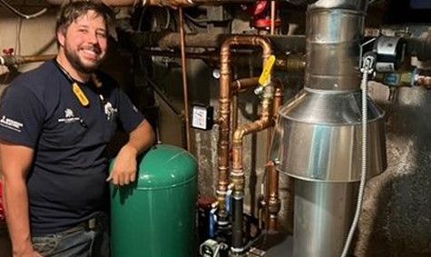 A man is standing in front of a water heater in a basement.