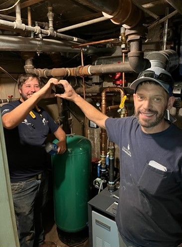 Two men are making a heart shape with their hands in a basement.