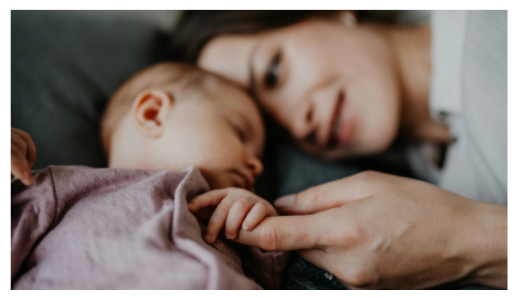 A woman is laying on a bed with a baby.