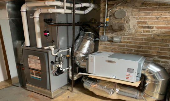A heating system is sitting in a basement next to a brick wall.