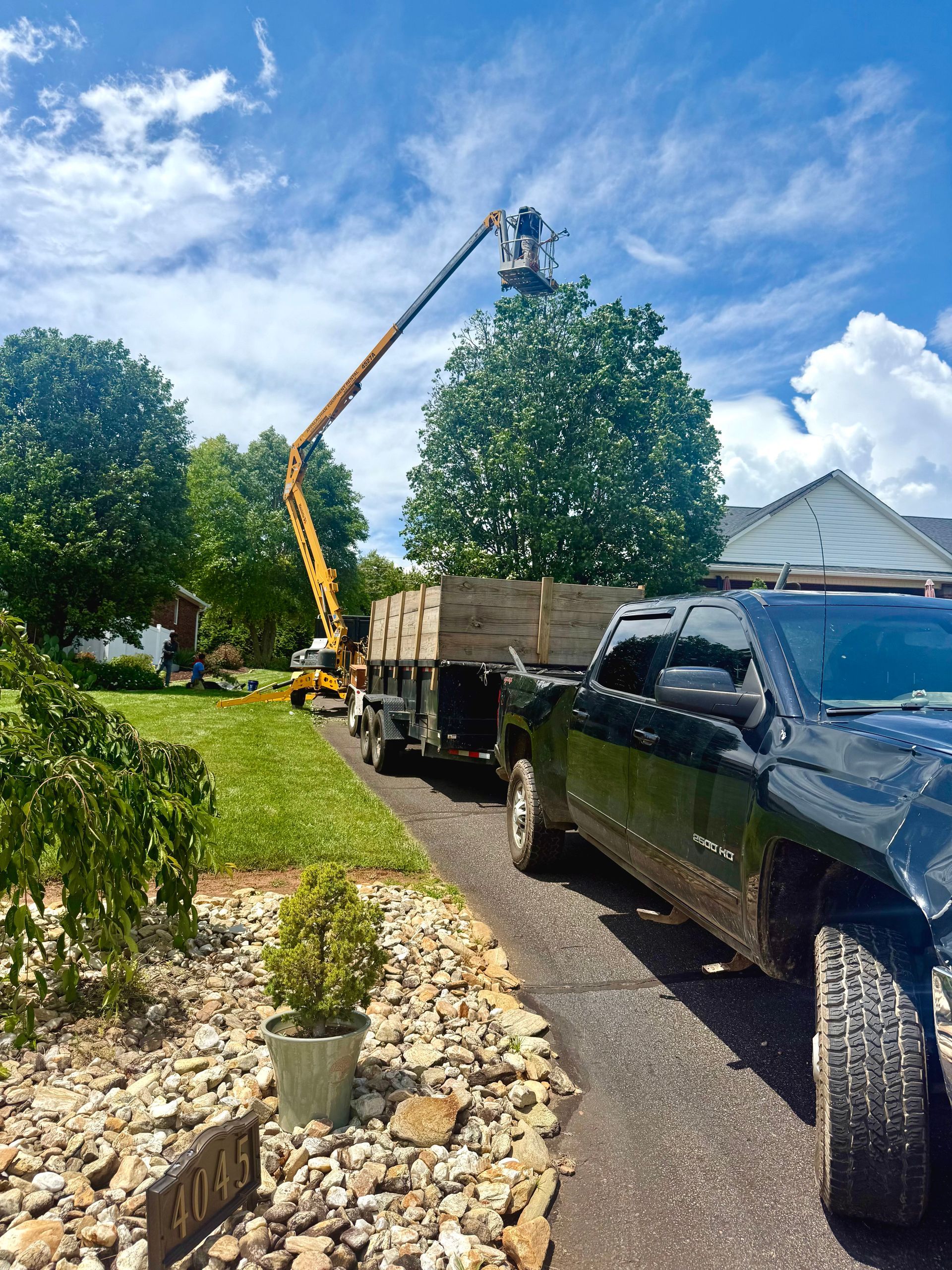 Truck and trailer with lift trimming a tree in a residential driveway.