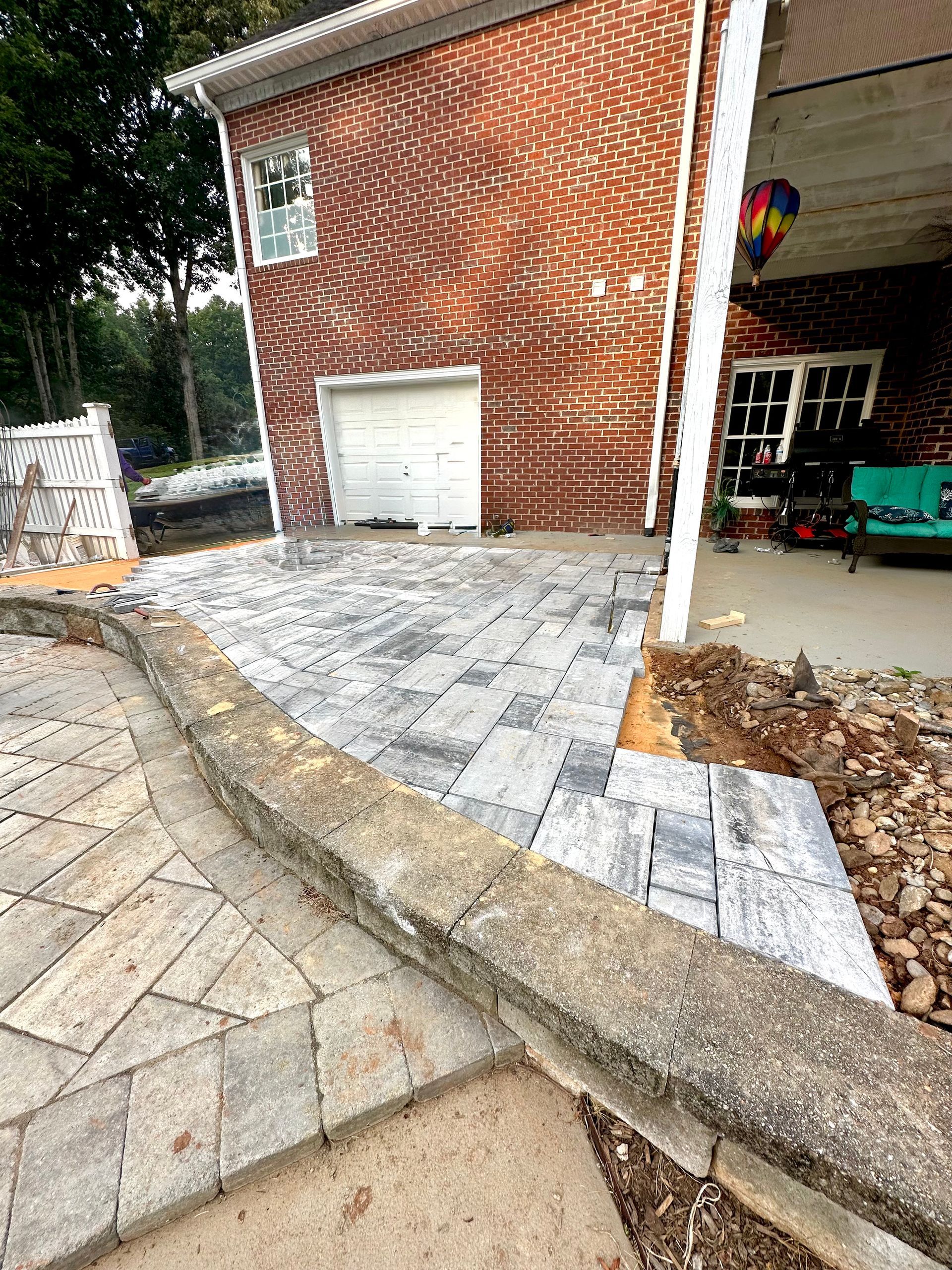 Brick building with new gray patio pavers, adjacent to an existing stone patio.