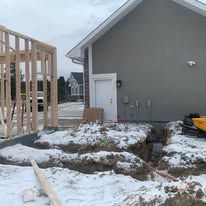 Construction site with snow, house, and wooden frame. Ground is dug up.