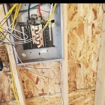 Electrical panel mounted on unfinished wood studs with exposed wires.