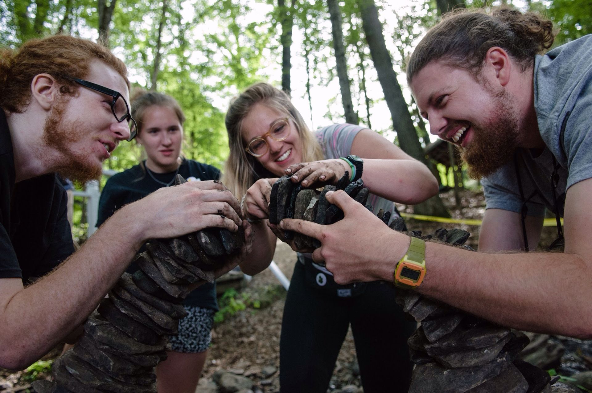 A group of people are looking at a camera in the woods.