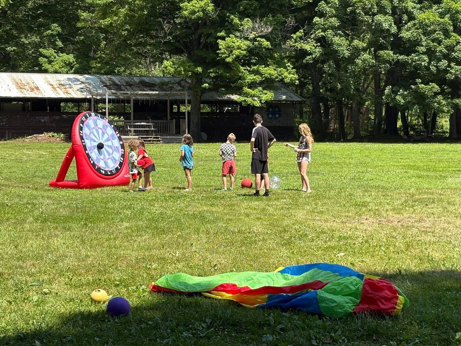 A group of children are playing in a field with a parachute and a dart board.
