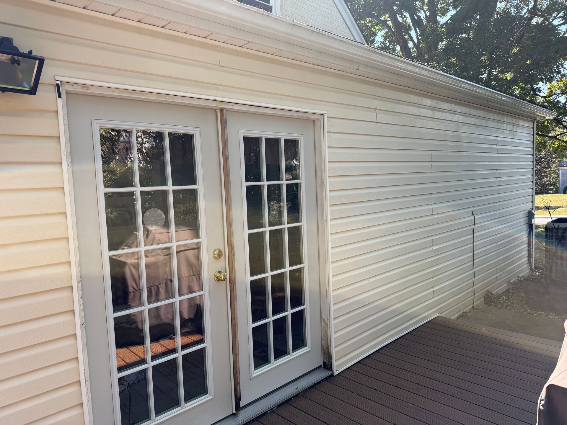 Man power washing a roof gutter with a pressure washer; blue sky and trees in the background.