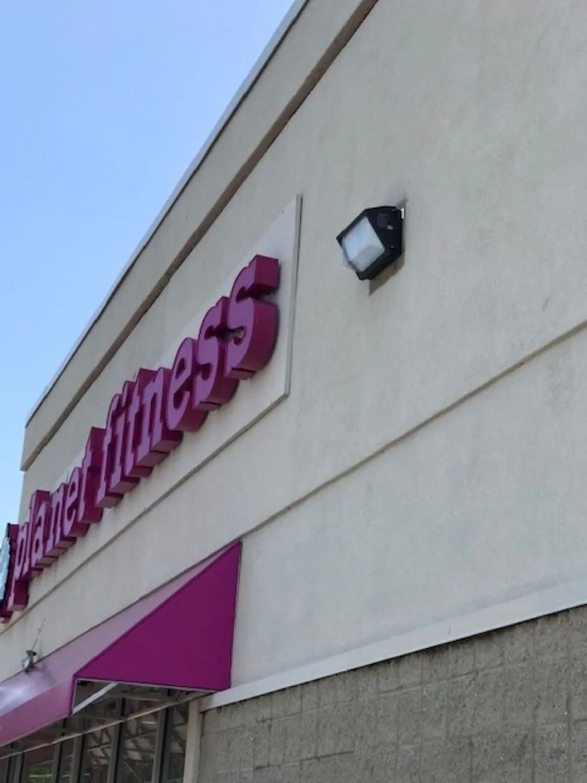Planet Fitness storefront with purple signage and awning, and a black light fixture.